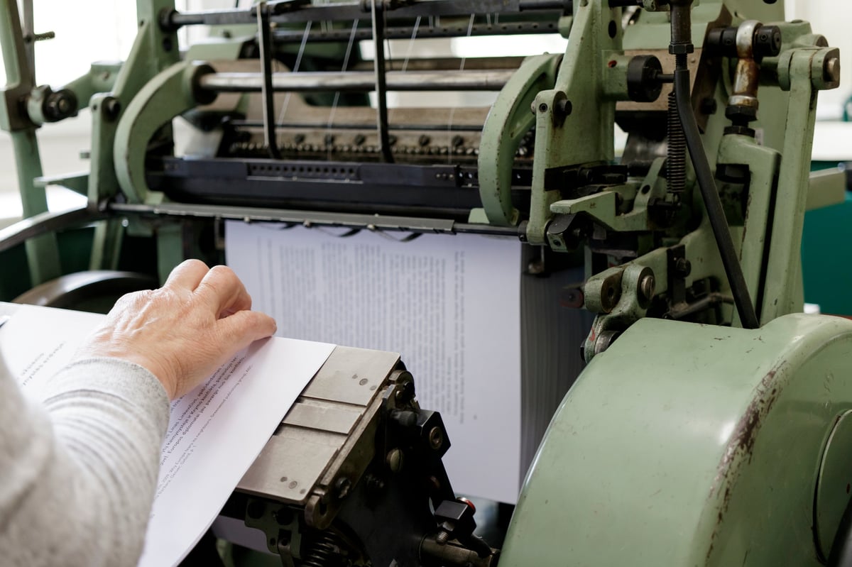 Machinery stitching book pages with thread in a bindery, with workers at the machine