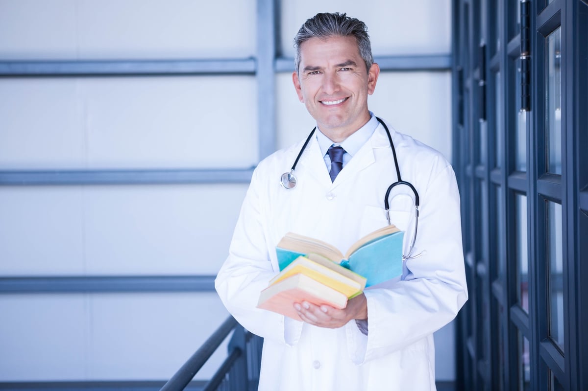 Portrait of a male doctor standing with a medical book in hospital